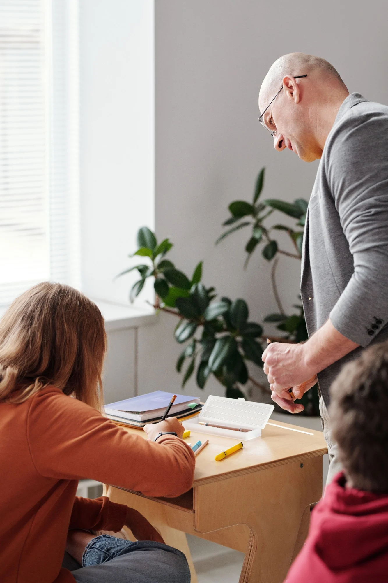 A teacher leaning over a student's desk to help with their work.
